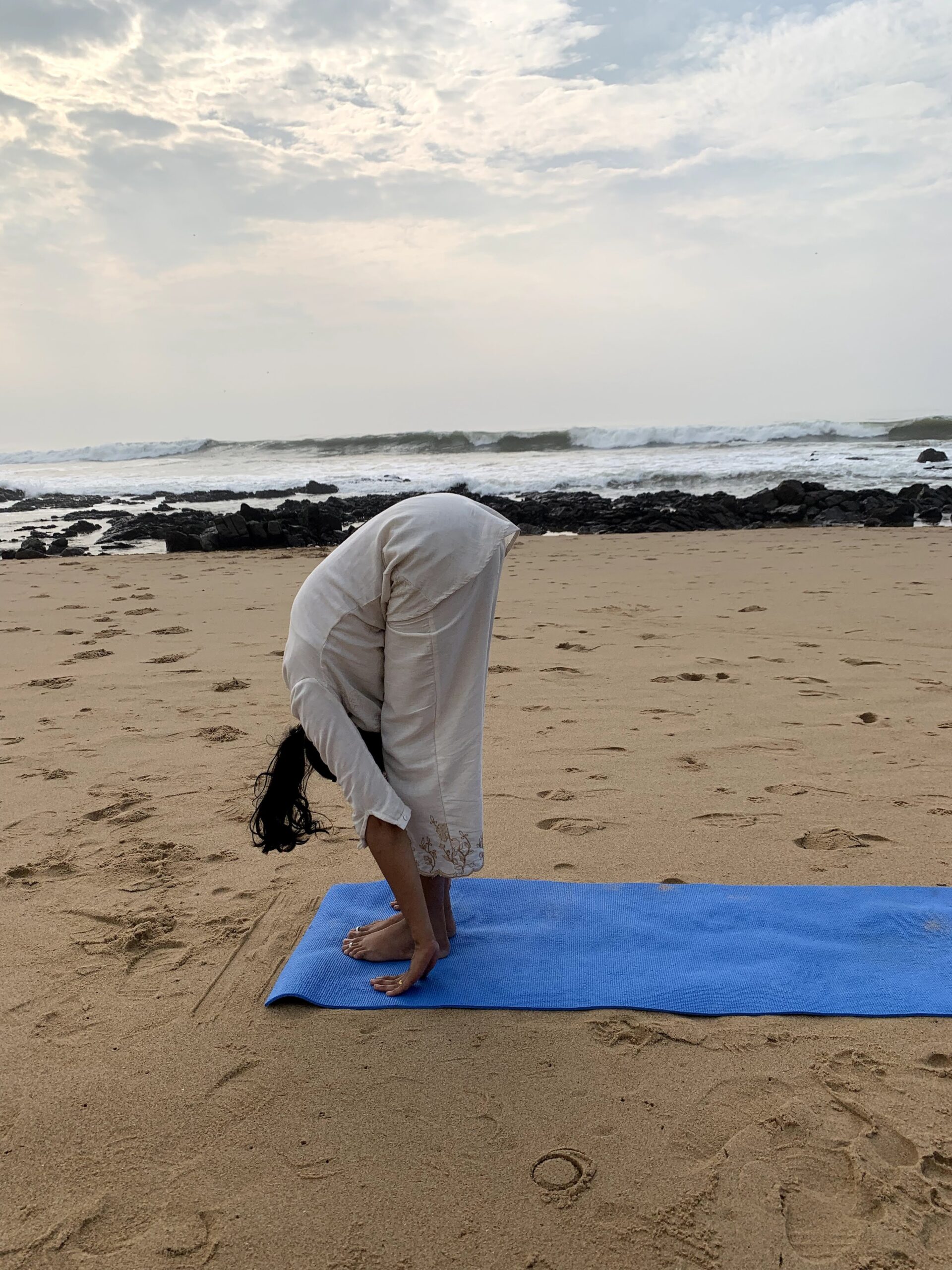 Practising a standing forward bend on a mat at sunrise